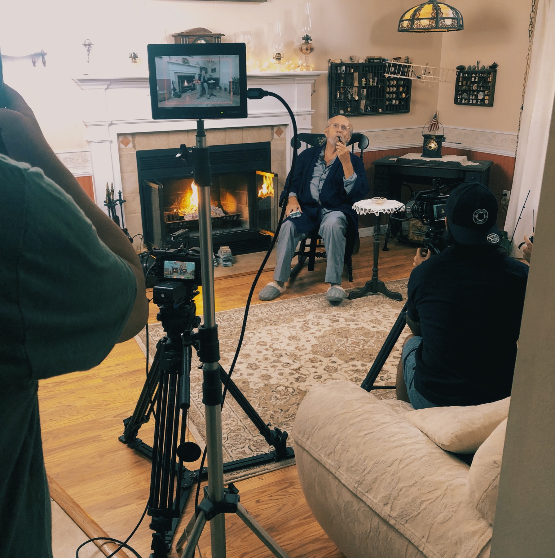 Cameras and a monitor set up to film a seated subject beside a fireplace